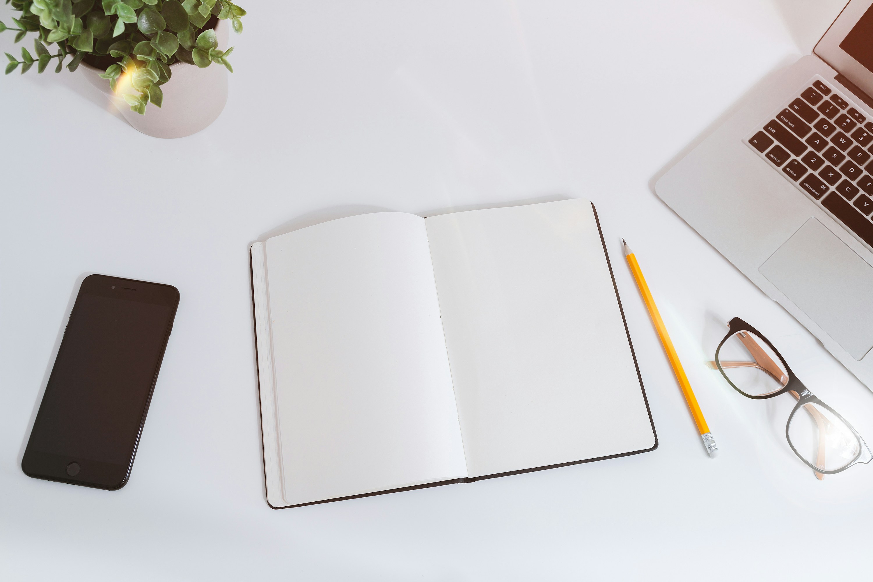 Caderno aberto entre um computador e um telefone sobre uma mesa de trabalho